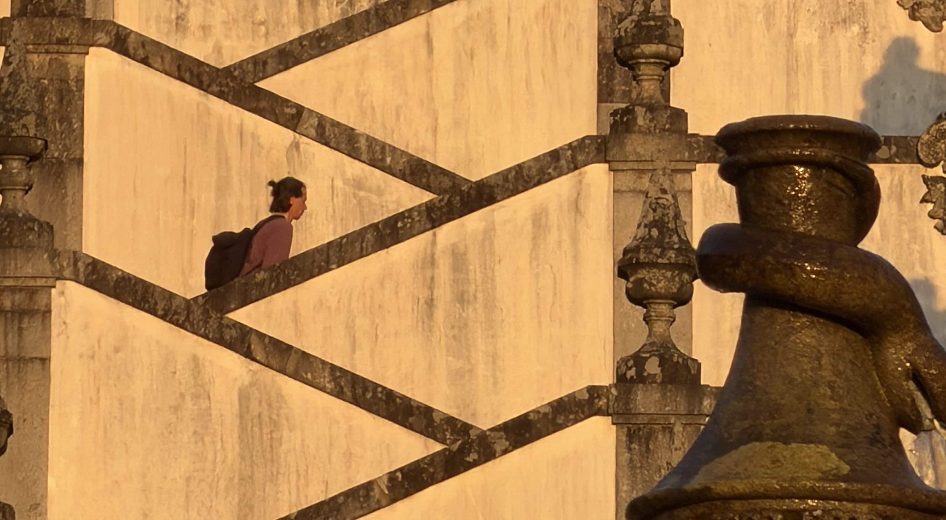 A lone figure climbing the geometric stone steps of a Portuguese monument at golden hour
